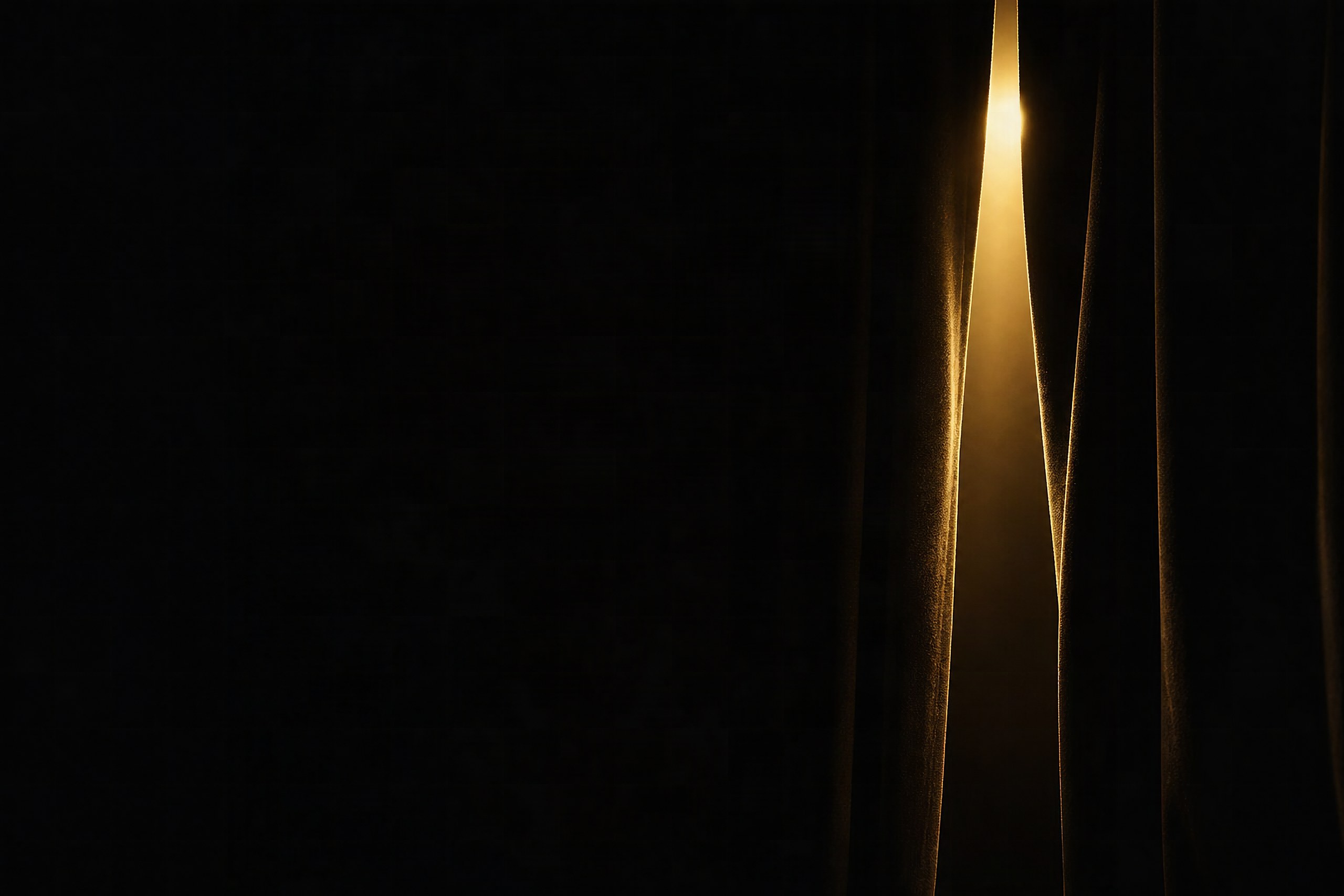 A stage curtain parted on a seam of warm light